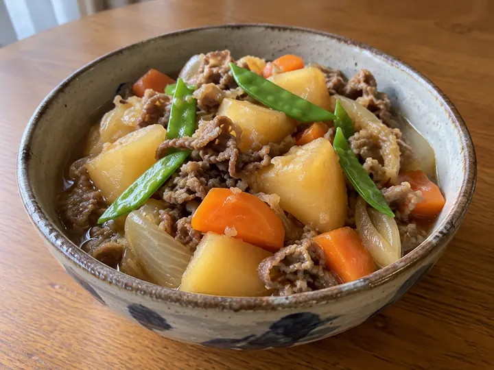木のテーブルに、染付けの鉢に盛った肉じゃが。じゃがいも、牛肉、玉ねぎ、にんじん、絹さや。